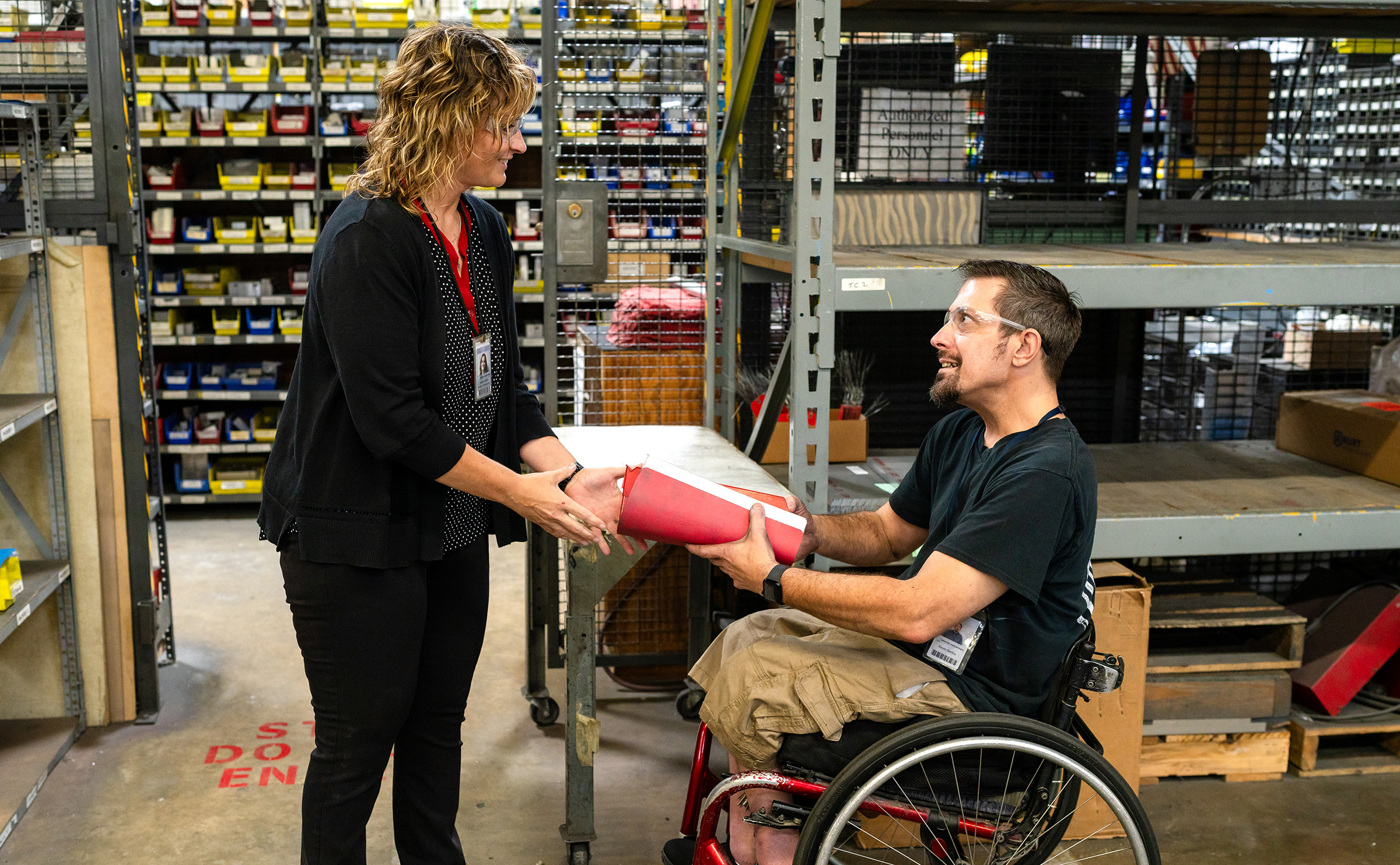 Man in wheelchair handing files to woman