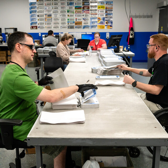 Group of people working on processing license plates for mail